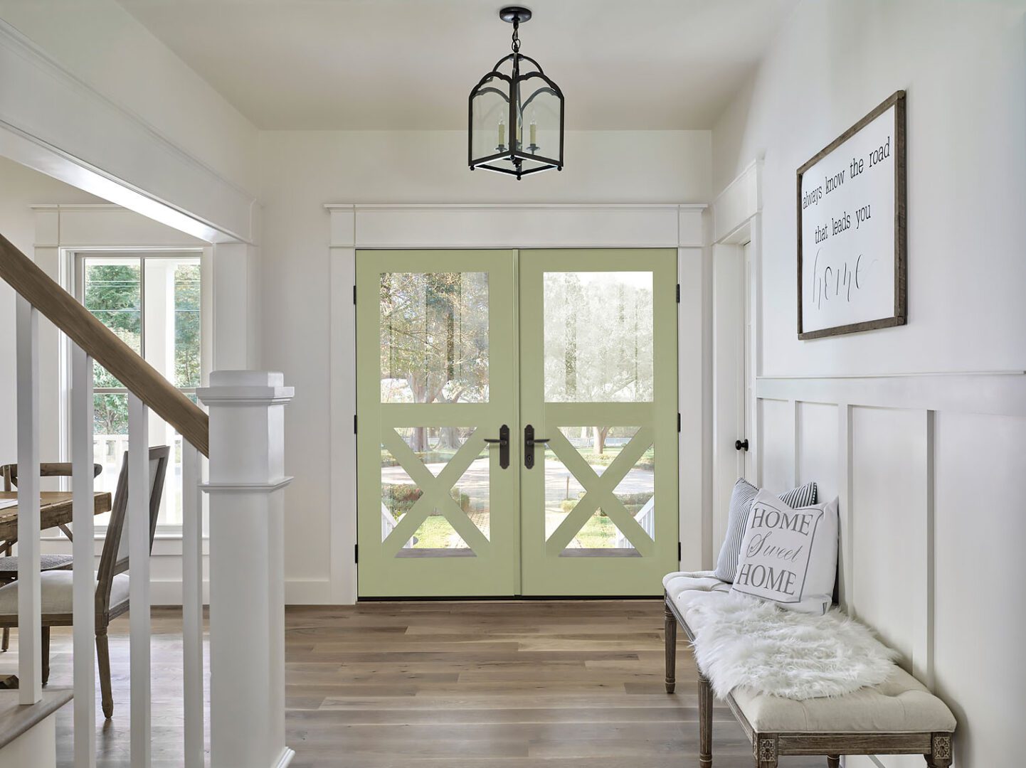 A bright, modern entryway featuring double barn doors with cross patterns, a wooden bench, and welcoming signs on the walls.